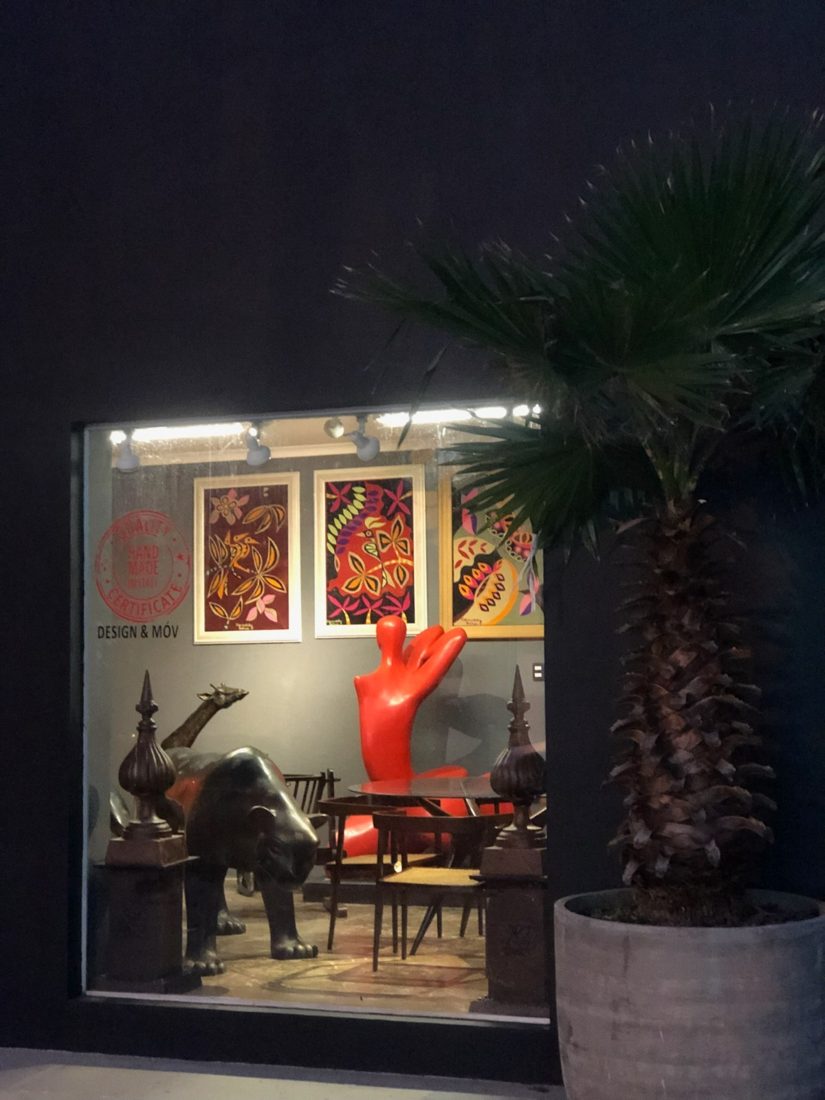 Vitrine da loja à noite, com escultura vermelha, felino em bronze e gravuras