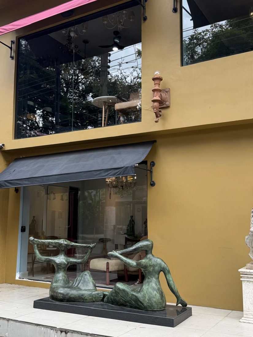 Fachada amarela da loja com toldo preto e escultura em bronze de duas figuras na calçada